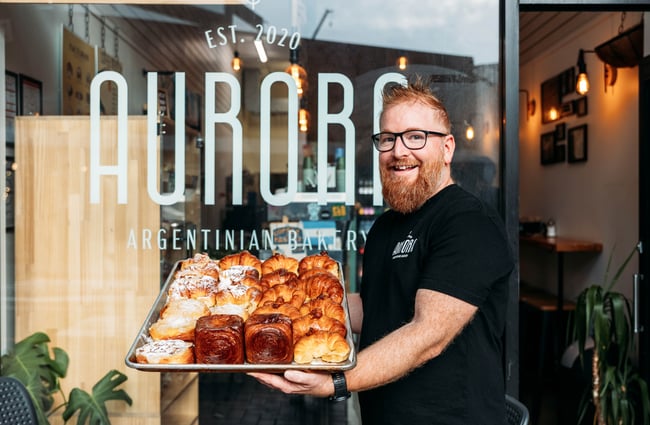 Baker holding a tray of pastries outside Aurora Argentinian Bakery.