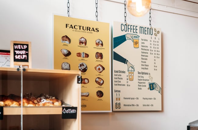 Coffee menu and other posters on the wall at Aurora Argentinian Bakery.