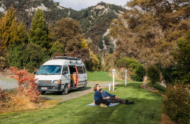 Two people sitting on grass next to a van at Awastone in Rangitikei.