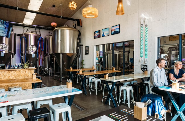 People sitting inside b.social with big, stainless steel vats at the back of the room.