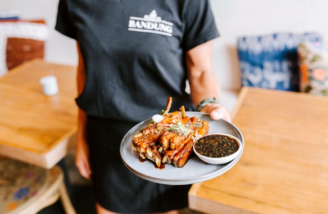 Woman holding a plate of ribs from Bandung Café, Auckland.