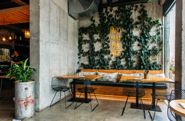 A wooden bench seat with an ivy covered wall behind it and a yellow neon sign.