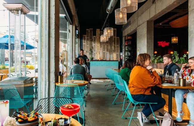 People sitting in the bright blue wire chairs around tables at the Banh Mi restaurant.