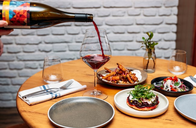 Wine being poured into a glass at a table full of plates of food.