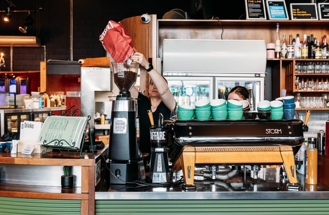 Barista pouring coffee beans into the hopper beside the coffee machine at Barista.