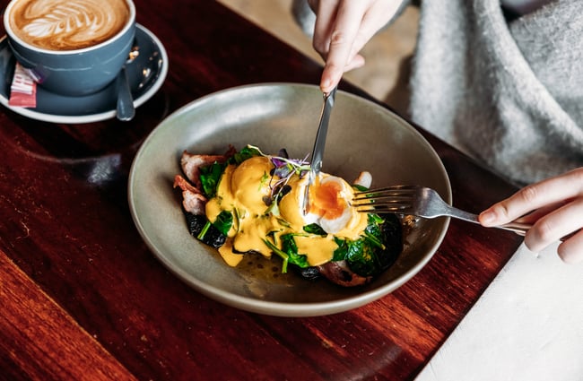 Customer cutting into a dish of Eggs Benedict at Barista.