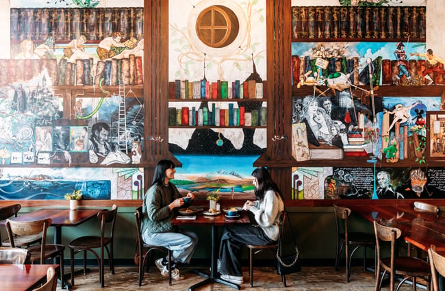 Two diners sitting at a table eating with lots of decorative  artwork behind them.
