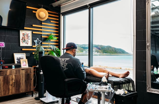 Legs splayed on a table whilst a man is receiving a tattoo.