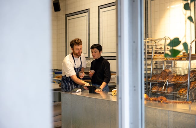 A man and woman behind the counter at a bakery.