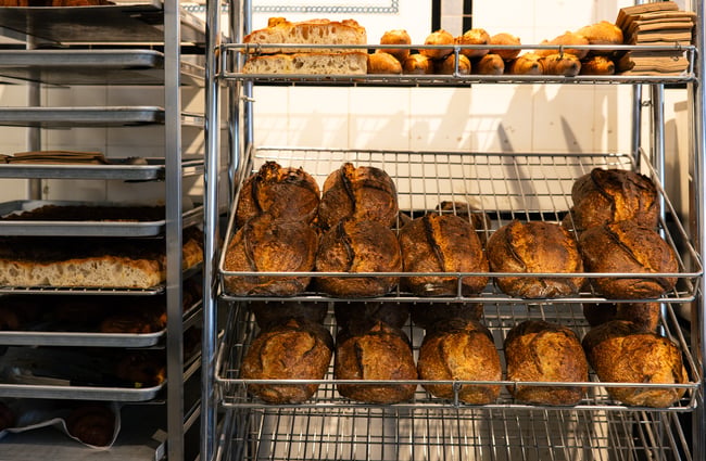 Loafs of sourdough on racks inside a bakery.