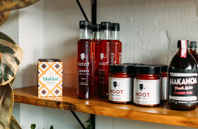 Sauces and jars on display on a wooden shelf.