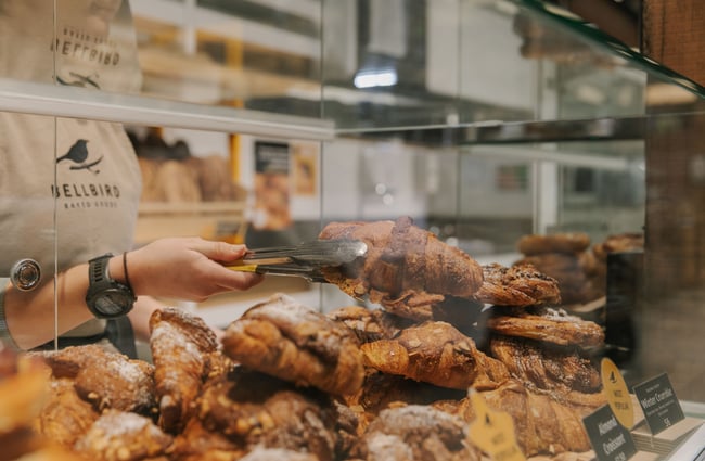 A close up of tongs holding on to a filled croissant inside a cabinet.
