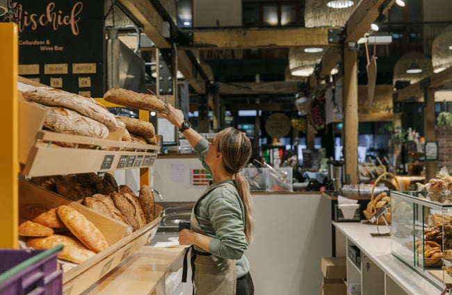 A woman reaching up for a loaf of bread.