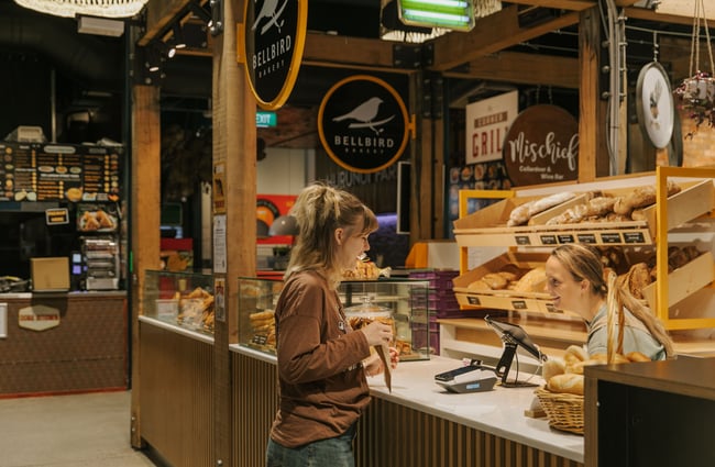 A customer and staff member chatting over a cafe counter.