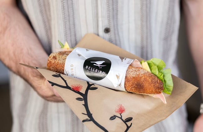 Customer holds a baguette sandwich at Bellbird Bakery Holmwood.