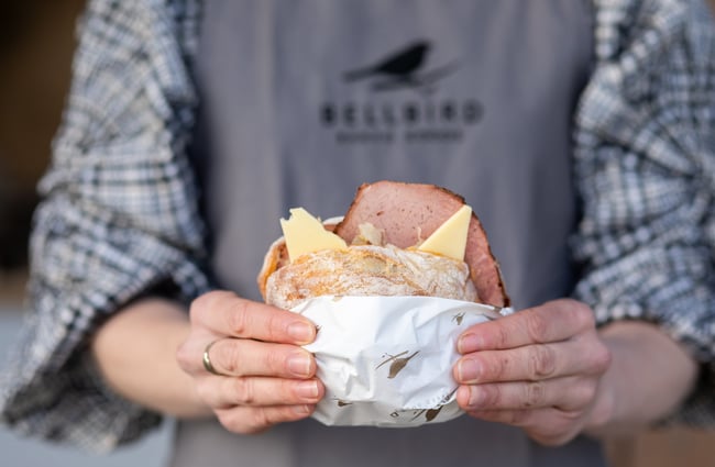 Bakery assistant holding a sandwich at Bellbird Bakery Holmwood.