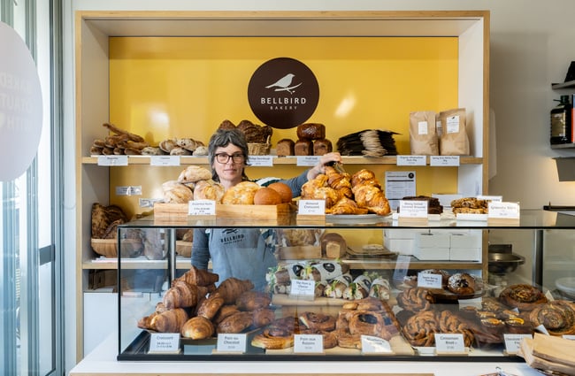 Bakery assistant stands behind the counter which is filled with pastries at Bellbird Bakery Holmwood.