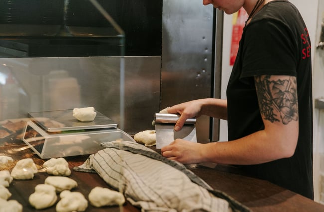 A baker dividing dough with a dough scraper.