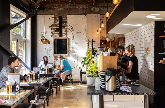 Baristas behind the coffee machine and customers sitting at tables.