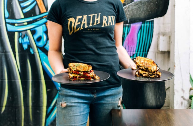 Woman holding two plates of toasted sandwiches.