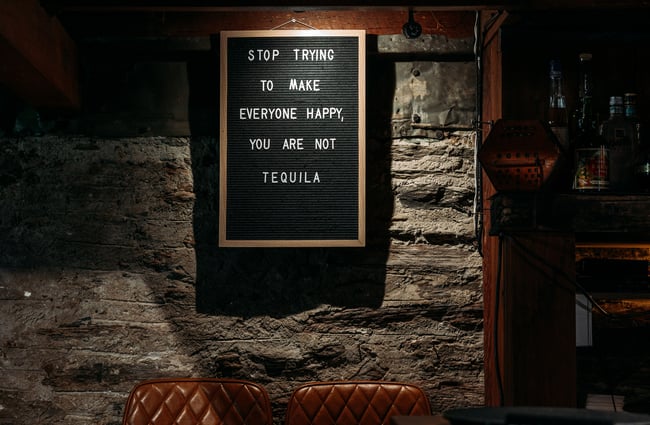 A black and white sign on a wall in a dark bar.