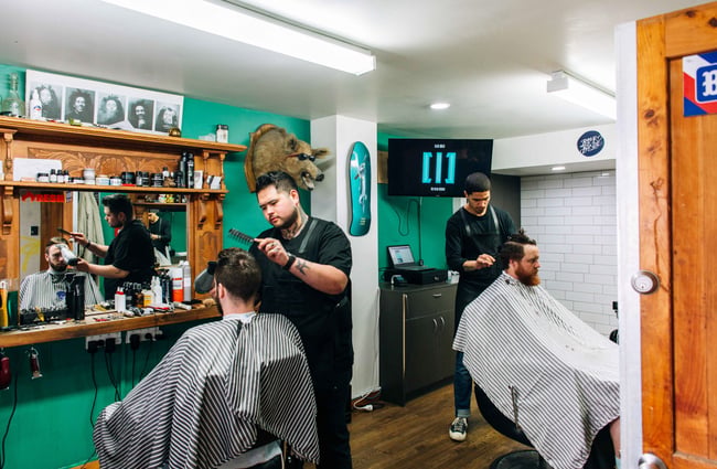 Two men getting a haircut in a green barber salon.