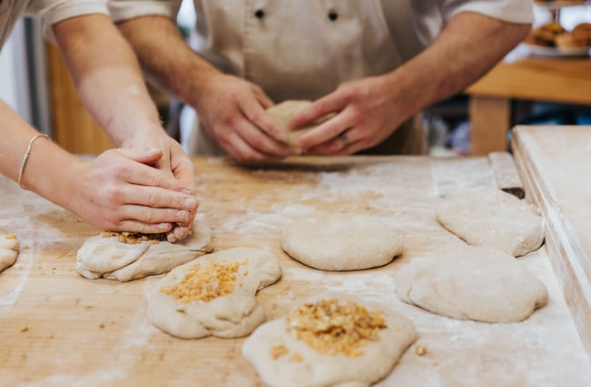 Bakers work with pastries on a wooden table.