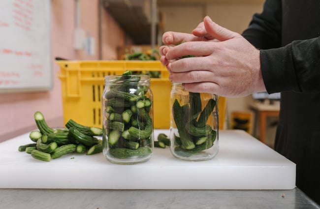 Chef adding cucumbers to the jar for Bones Pickles.