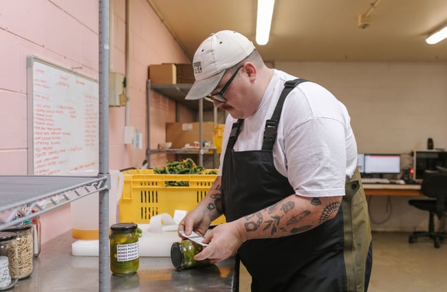 Chef adding a label to a jar at Bones Pickles.