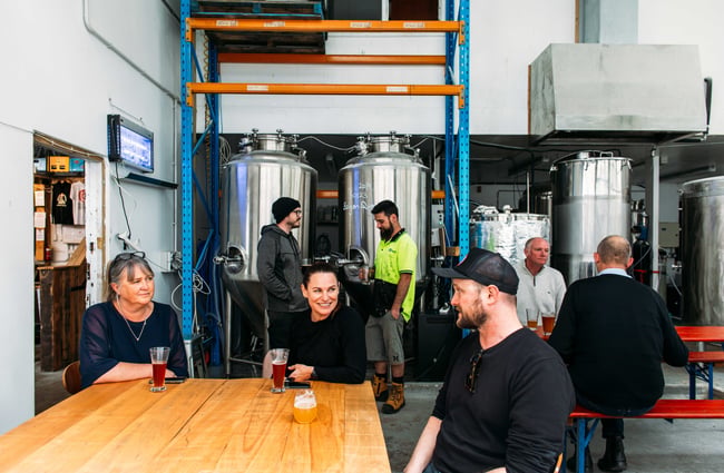 Three people sitting around a big wooden table with glasses on beer.