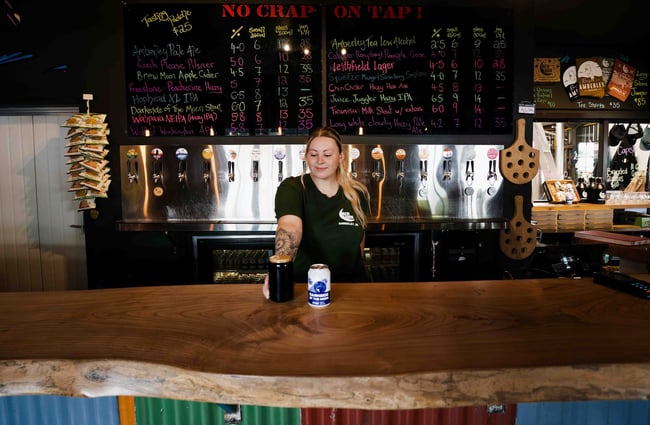 A bartender puts as a pint of stout and a can on the bar counter at Brew Moon.