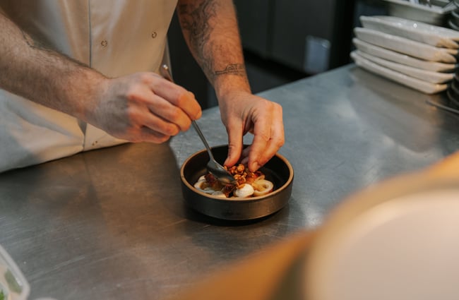 Hands preparing a meal in a commercial kitchen.