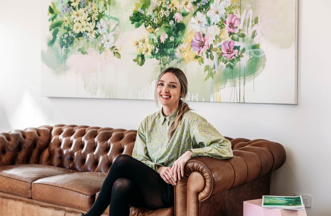 A woman sitting on a brown couch smiling to camera.