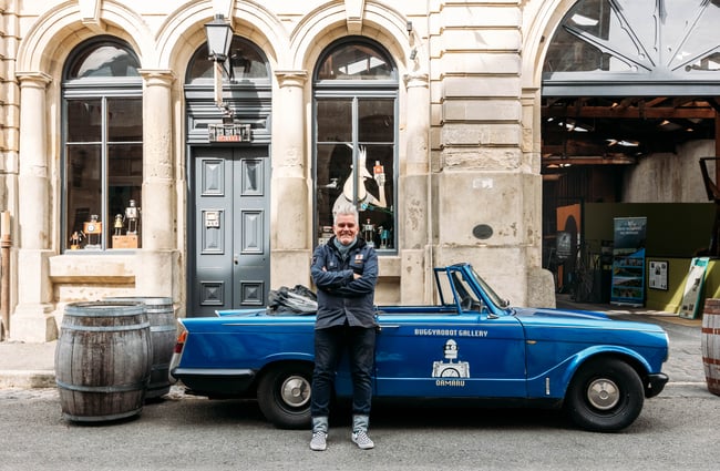 Owner of Buggyrobot Martin Horspool standing in front of blue convertible car outside Buggyrobot in Ōamaru