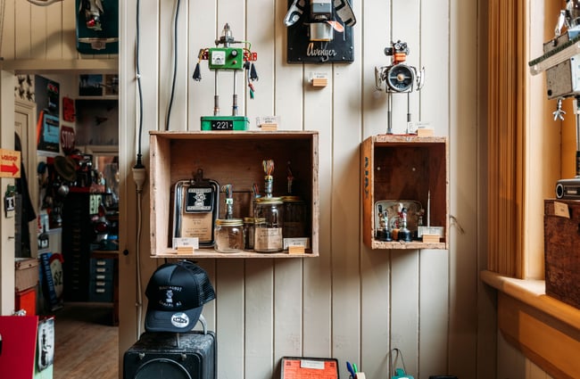 Old wooden crates used as shelves on wall to display a green and silver robot sculpture and glass jars with robot heads