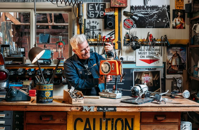 Martin Horspool working on orange robot sculpture at his workshop desk inside Buggyrobot in Ōamaru