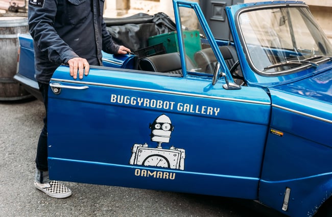 Close up of blue convertible car with 'Buggyrobot Gallery' written on the driver door