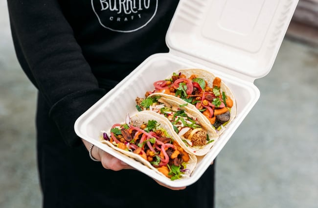 A hand reaching for the middle of three tacos in a box.