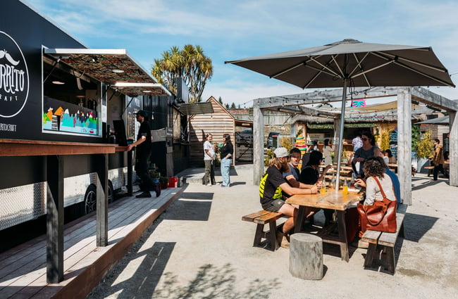 People waiting and eating at the outdoor tables by the food truck.