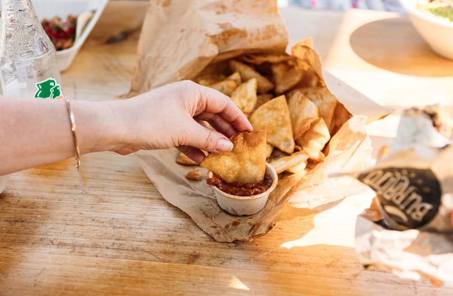 A hand dipping a corn chip in thick, red salsa.