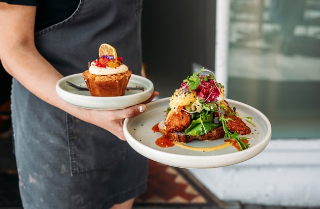 Close up of waitstaff holding a savoury brunch plate and a cake on another plate.