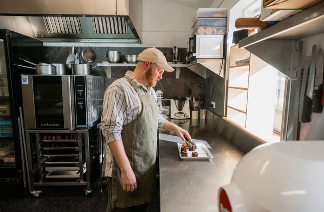 A man working inside a kitchen holding onto a pastry with a pair of tongs.