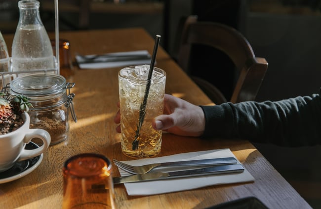 Close up of a customer’s outstretched arm at a table holding onto a glass of soda.