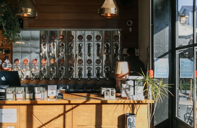 Stainless steel wall bulk bins behind a wooden counter at C4 housing their wide selection of coffee beans for purchase.