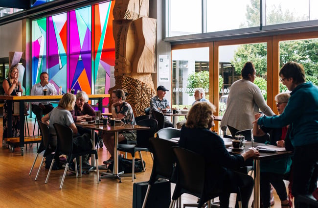 Cafe patrons enjoying a meal and coloured stained glass window behind.