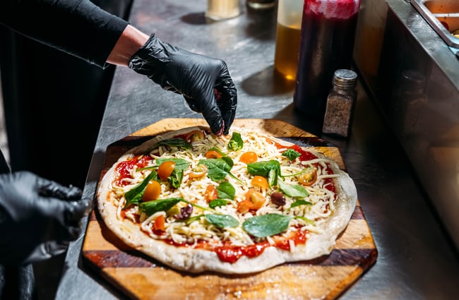 Pizza toppings being added by a chef in the kitchen at Cambridge Lane.