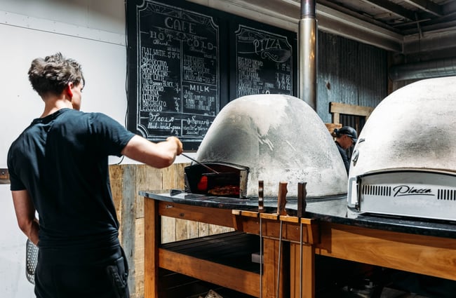 Chef is putting a pizza into the pizza oven in the kitchen of Cambridge Lane.