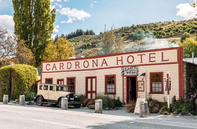 Historic cream and maroon weatherboard frontage of Cardrona Hotel with a vintage cream 1968 Chrysler Model 62 parked in front.