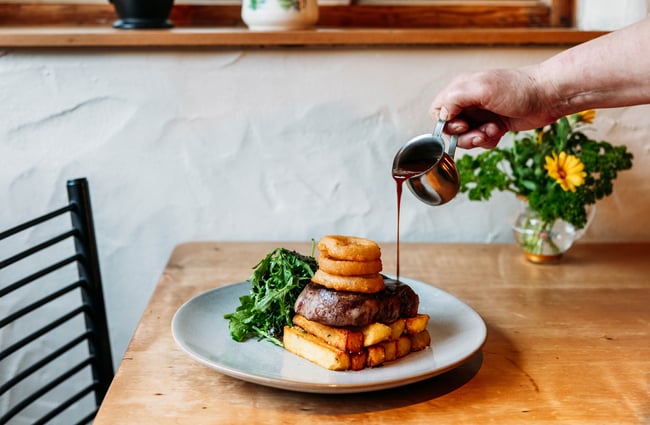 A person pours gravy over a savoury dish at Cardrona Hotel.