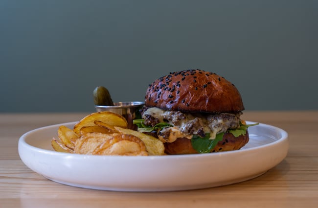 A burger and housemade chips on a plate with a pickle.